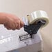 A hand using a Shurtape Deluxe Silencer Pistol Grip tape dispenser to seal a box.