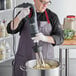 A man in a chef's uniform using an AvaMix heavy-duty immersion blender with a whisk attachment to mix food.