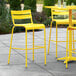 A yellow Lancaster Table & Seating outdoor bar stool on a concrete patio.