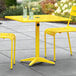 A yellow Lancaster Table & Seating outdoor table with two chairs.