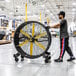 A man pushing a large black Big Ass Fans portable floor fan in a warehouse.
