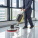 A man in a blue uniform using a Lavex single speed rotary floor machine to clean a floor.