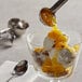 A spoon pouring I. Rice pineapple dessert topping onto a glass of ice cream.