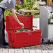 A man placing a bottle of beer in a red CaterGator outdoor cooler.