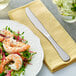 A plate of shrimp and vegetables on a napkin next to an Acopa Vittoria stainless steel dinner knife.