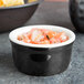 A black Tuxton ramekin filled with salsa next to a bowl of chips on a table.