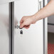 A hand using a key to unlock a cabinet drawer.