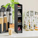 A ServSense black countertop condiment organizer holding cups and bottles on a table.