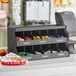 A black ServSense countertop condiment organizer with 12 sections on a counter.