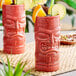 Two red Libbey tiki tumblers with fruit and straws.