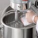 A hand pouring liquid into a metal container using an Avantco stand mixer.