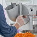 A person using an Avantco Planetary Stand Mixer to cut carrots.