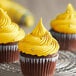 Three cupcakes with LorAnn Oils yellow frosting on a metal rack.