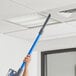 A person using a blue Lavex stick vacuum to clean a ceiling.