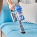 A hand using a Lavex Pro cordless stick vacuum to clean a couch.