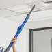 A person using a blue Lavex Pro cordless stick vacuum to clean the ceiling.