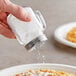 A hand using a Tablecraft clear glass mason jar shaker to sprinkle powdered sugar on food.
