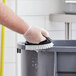 A gloved hand using a Lavex black iron scrub brush to clean a grey container.