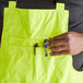 A person holding a tool in a hi-vis lime bib pant pocket.