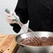 A person using a Vollrath stainless steel whisk to mix chocolate batter in a bowl.