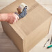A hand using a tape dispenser to open a Lavex cardboard shipping box.