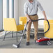 A man using an Atrix canister vacuum to clean a yellow chair.