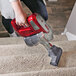 A person using a red and silver Atrix cordless stick vacuum to clean carpeted stairs.