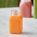 A 4 oz square PET clear juice bottle filled with orange juice on a table in a juice bar.