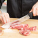 A person using a Victorinox butcher knife to cut meat on a wooden cutting board.