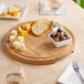 A Boska round oak serving board with cheese, bread, and olives on a table.