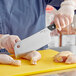 A person using a Kai Pro cleaver to cut chicken on a cutting board.