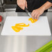A person using a Tablecraft white flexible cutting board to cut a yellow bell pepper.
