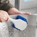 A hand using a blue Lavex pot scrub brush to clean a metal container.
