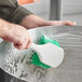 A hand using a Lavex green utility brush to clean a metal bowl on a counter.
