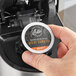 A hand holding a round black and orange container of Ellis Mezzaroma Decaf Royal Sumatra coffee pods.