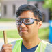 A man wearing Honeywell Uvex Tirade safety glasses and a reflective vest holding a wooden stick.