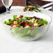 An Arcoroc clear glass bowl filled with salad on a table.