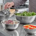 A person using a Choice stainless steel mixing bowl to make salad at a table with other bowls of salad.