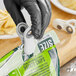 A hand in a black glove using an OXO white magnetic clip to close a bag of potato chips.