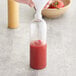 A hand pouring tomato sauce into a 16 oz. Cosmo Bullet PET clear bottle.