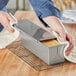 A person using a Chicago Metallic aluminized steel loaf pan with a cover to bake bread.