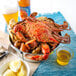 A bowl of extra seasoned steamed blue crab with corn on a table with a blue cloth and a glass of beer.