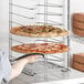 A person holding a pizza on a Choice aluminum pizza pan rack.