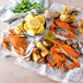 A Chesapeake Crab Connection bushel of seasoned steamed blue crabs with corn on the cob and lemon wedges on a table.