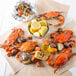 A bushel of large and extra large steamed blue crabs with corn on the cob and potatoes on a table.