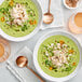 A group of bowls of green soup with Chesapeake Crab Connection Jumbo Lump Blue Crab Meat and vegetables.