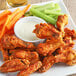 A plate of chicken wings and vegetables with a bowl of dip.