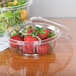 A Dart clear plastic bowl filled with strawberries sitting on a table.