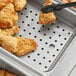 A stainless steel tray filled with fried chicken on a table with a black false bottom.
