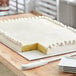 A white full sheet cake on a white corrugated cake board with a slice missing.